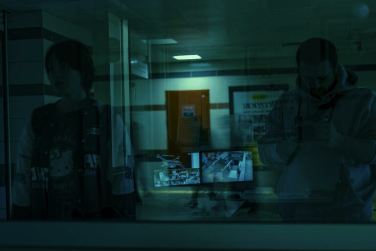 Shadowy figures reflected with security monitors in the foreground.